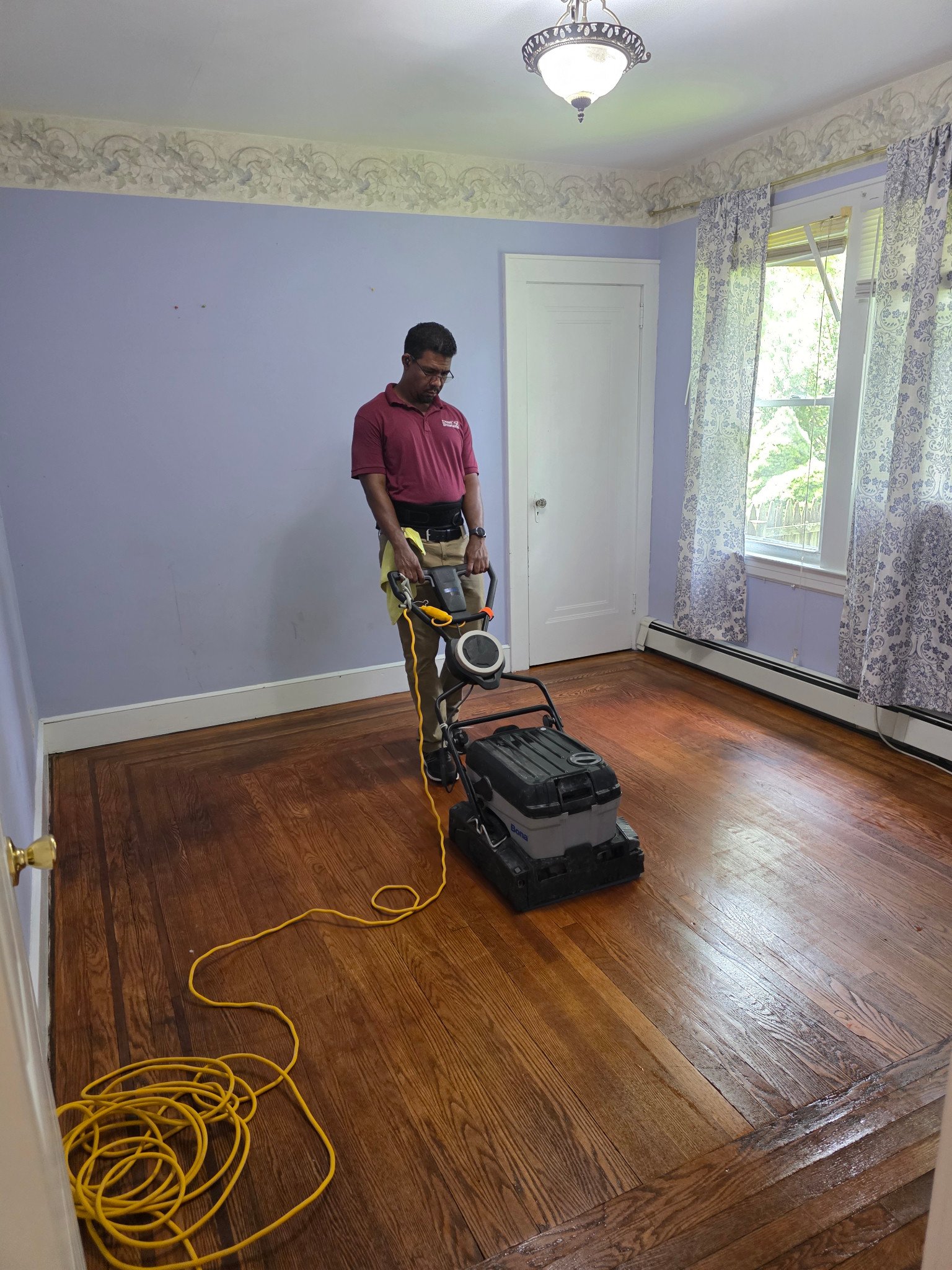 Dust Busters team member using a floor-cleaning machine on a hardwood floor.