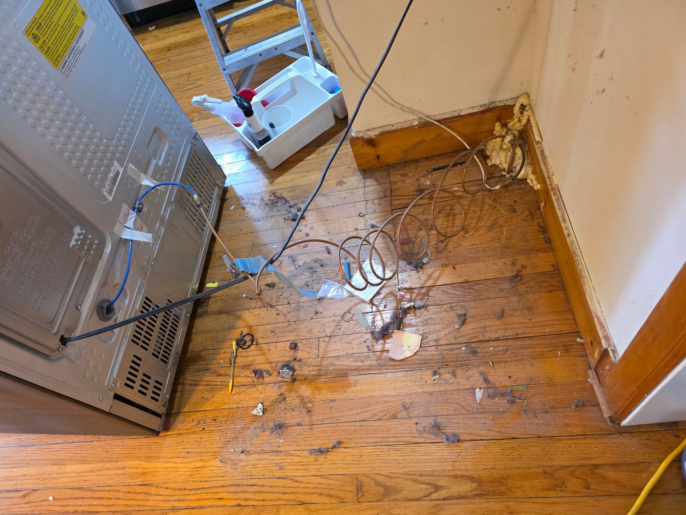 Dust and debris on a wood floor behind a refrigerator during a residential deep-cleaning visit
