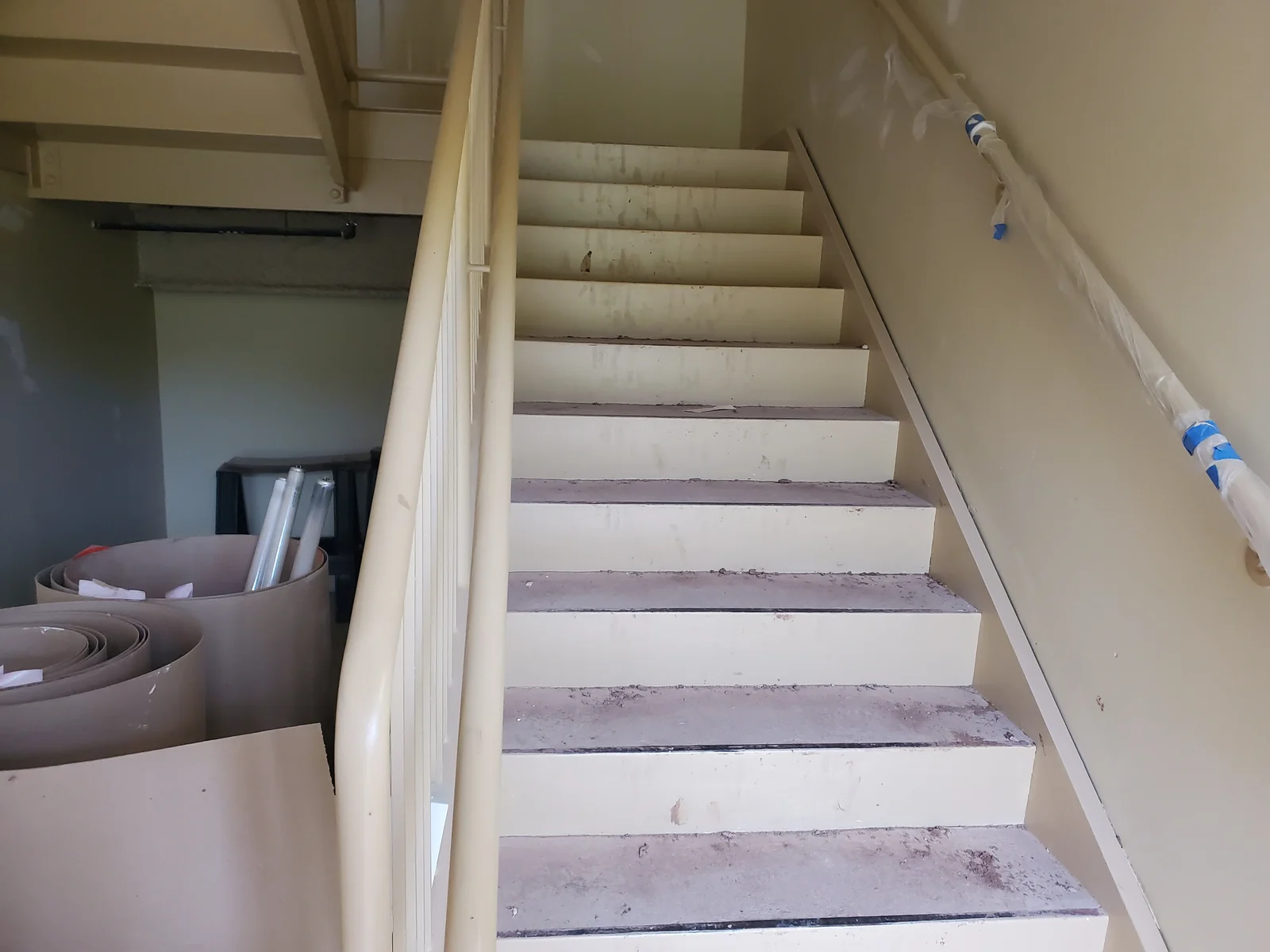 Dust and debris on interior stairs beside a wrapped handrail.