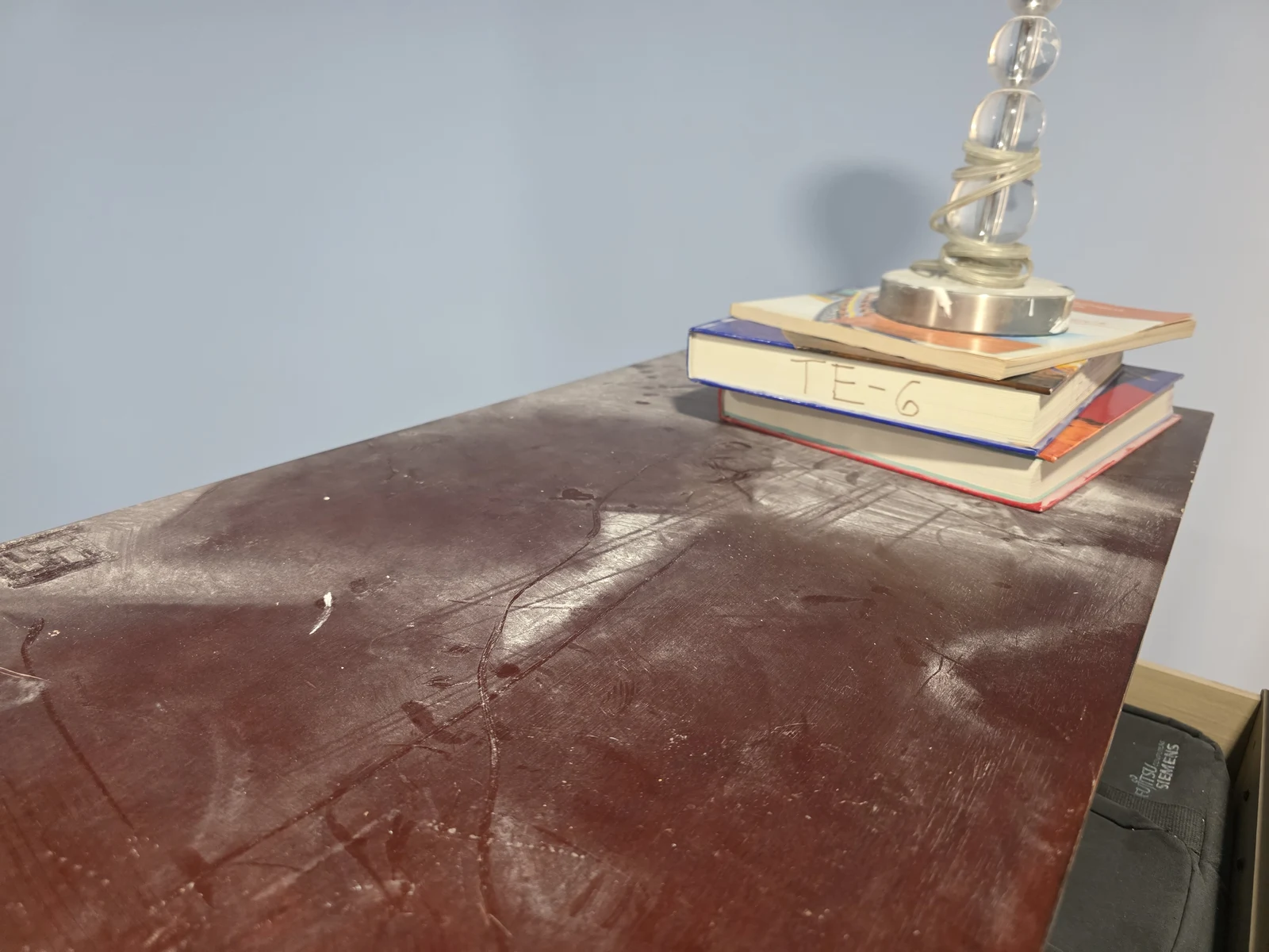 Dust on a dark tabletop beside a lamp and stacked books.