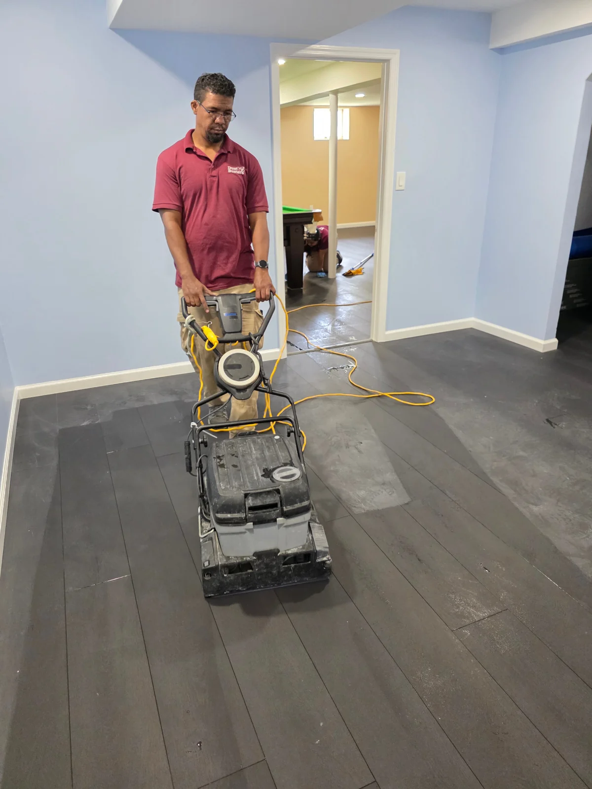 Dust Busters team member operating a floor-cleaning machine on a dark gray LVT plank floor.