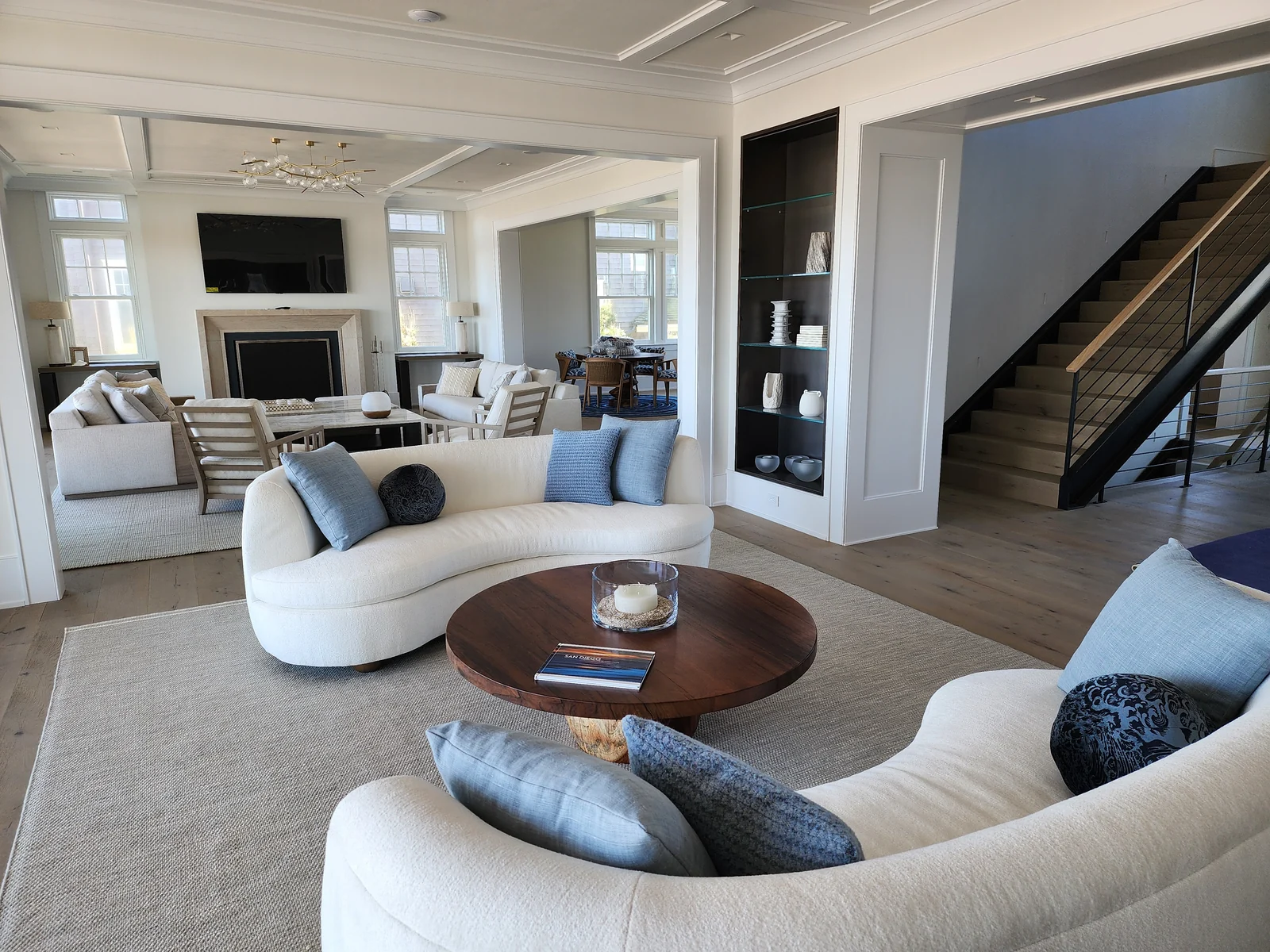 Furnished living room with white sofas, a fireplace and an adjoining staircase.