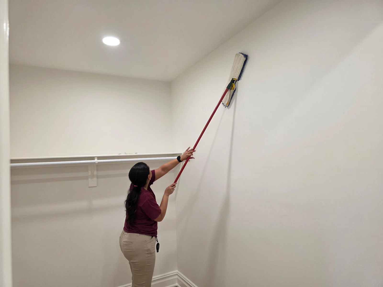 Worker using an extension pole to dust a wall.