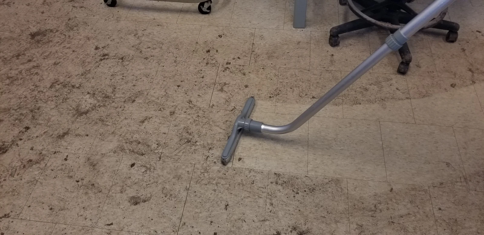 Vacuum attachment removing debris from a floor beside office-chair wheels.