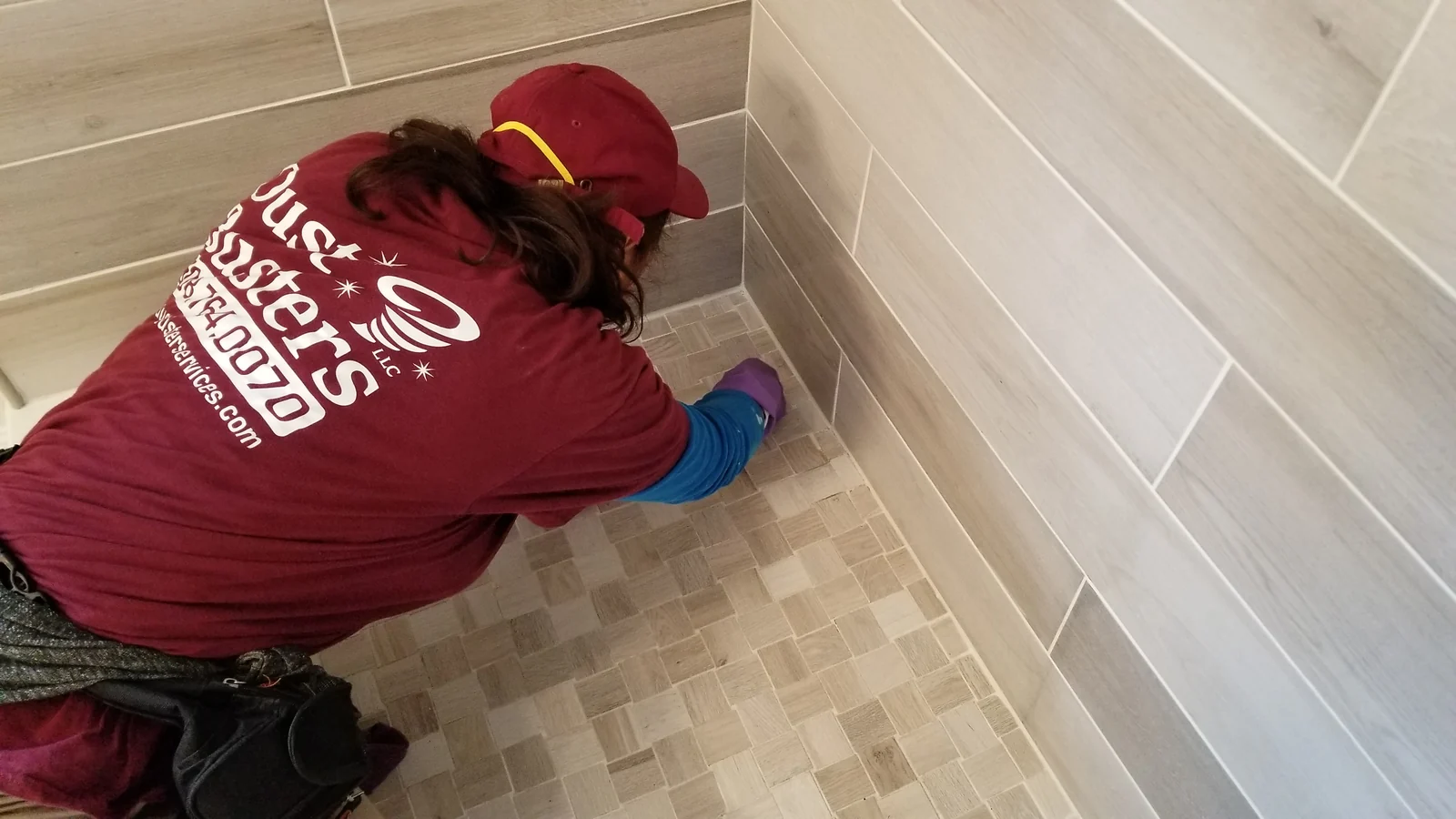 Worker cleaning tile along the corner of a shower.