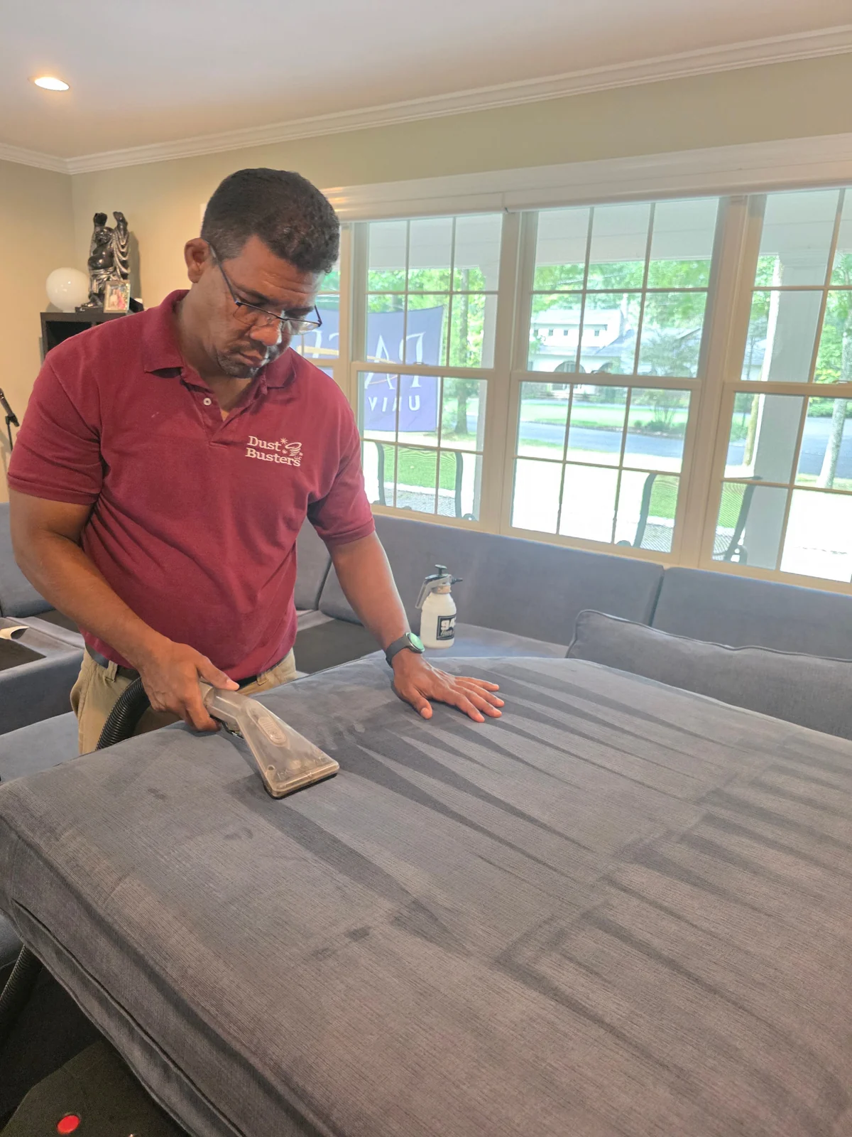 Dust Busters worker using an extraction tool on gray upholstery